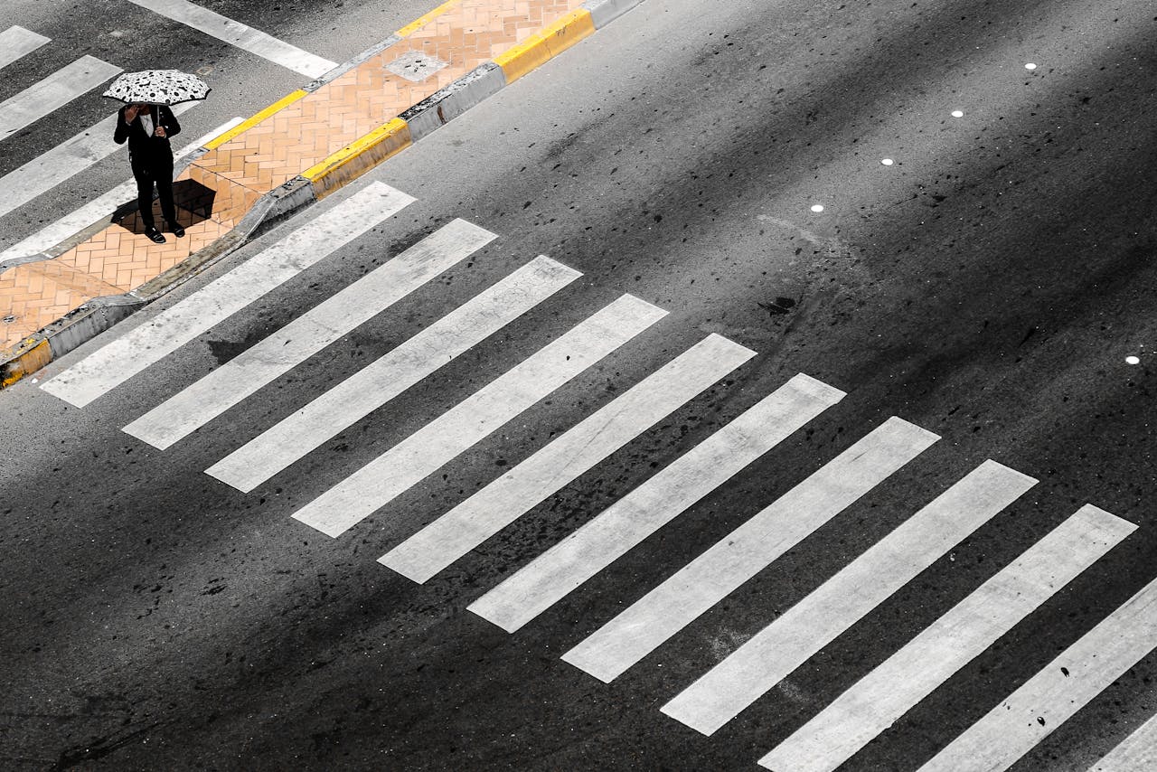 Aerial view of a lone pedestrian with an umbrella at a crosswalk in Abu Dhabi.