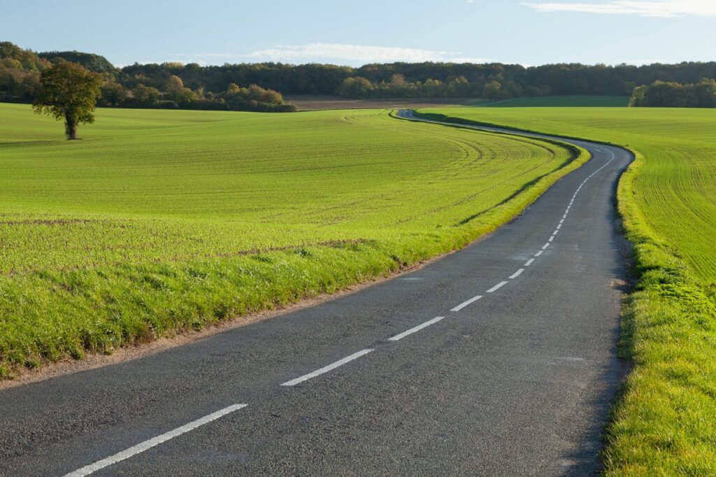 A picturesque roadway winding through lush fields in Gommecourt, France, during fall.